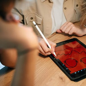 A person creatively designs a Halloween-themed illustration on a tablet using an Apple Pencil. Indoors setting.